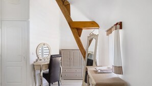 A room with a white door, a vanity with a mirror, a chair, a dresser, and a table with a cloth.