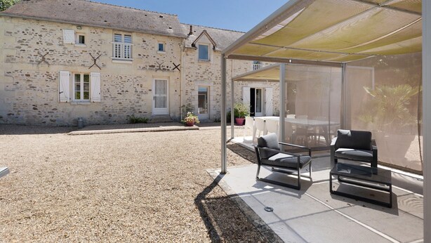 A stone building with a covered outdoor seating area and a gravel driveway.