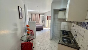 A compact hotel room with a kitchenette, a dining area with a table and chairs, and a bed in the background. - Golden Thermas Residence (Caldas Novas)