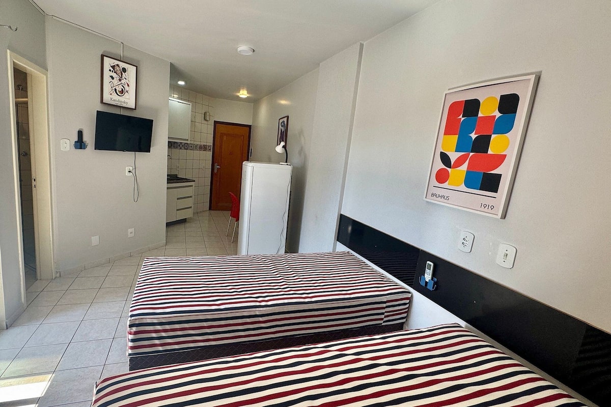 A hotel room with a bed, a small kitchenette, a TV, and a door leading to a bathroom.