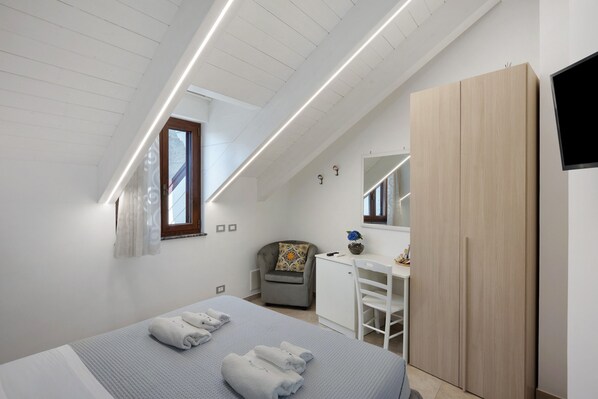 A bedroom with a bed, a desk, a chair, a wardrobe, and a window.