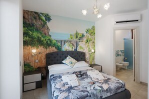 A bedroom with a bed, nightstands, a wall mural, a ceiling light, and an air conditioning unit. - Room 'Le 5 Perle - Furore' with Mountain View, Wi-Fi and Air Conditioning (Agerola)