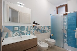 A bathroom with a white sink, bidet, toilet, and a shower area with blue tiles. - Room 'Le 5 Perle - Furore' with Mountain View, Wi-Fi and Air Conditioning (Agerola)