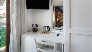 A hotel room with a white desk, a flat-screen TV mounted above it, a small vase with flowers, a coffee maker, and a remote control. - Room 'Le 5 Perle - Positano' with Mountain View, Wi-Fi and Air Conditioning (Agerola)