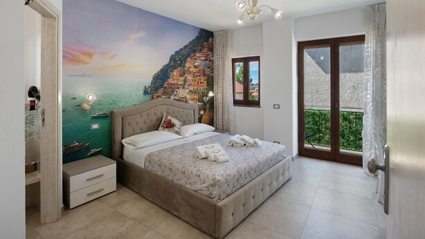 A bedroom with a mural of a coastal scene, a bed with towels, a nightstand, and a window with a view. - Room 'Le 5 Perle - Positano' with Mountain View, Wi-Fi and Air Conditioning (Agerola)