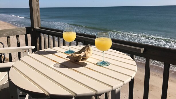Een tafel met twee glazen sinaasappelsap op een houten terras met uitzicht op de oceaan.