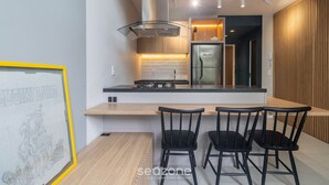 Une cuisine moderne avec un îlot central, des chaises noires et une œuvre d’art encadrée au mur.
