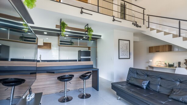 Une cuisine moderne avec un îlot central, des tabourets de bar, un canapé et un escalier.
