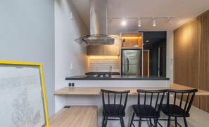 A modern kitchen with a central island, black chairs, and a framed artwork on the wall. - YHD - Condominium With Pool Near Ufsc Located in Carvoeira, This Condominium is an Excellent Choi (Florianópolis)