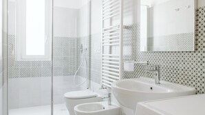 Un baño moderno con cabina de ducha de vidrio, inodoro, bidé, lavamanos y lavadora.