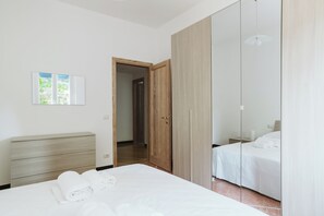 A modern bedroom with a large bed, a wooden wardrobe, and a mirror cabinet.