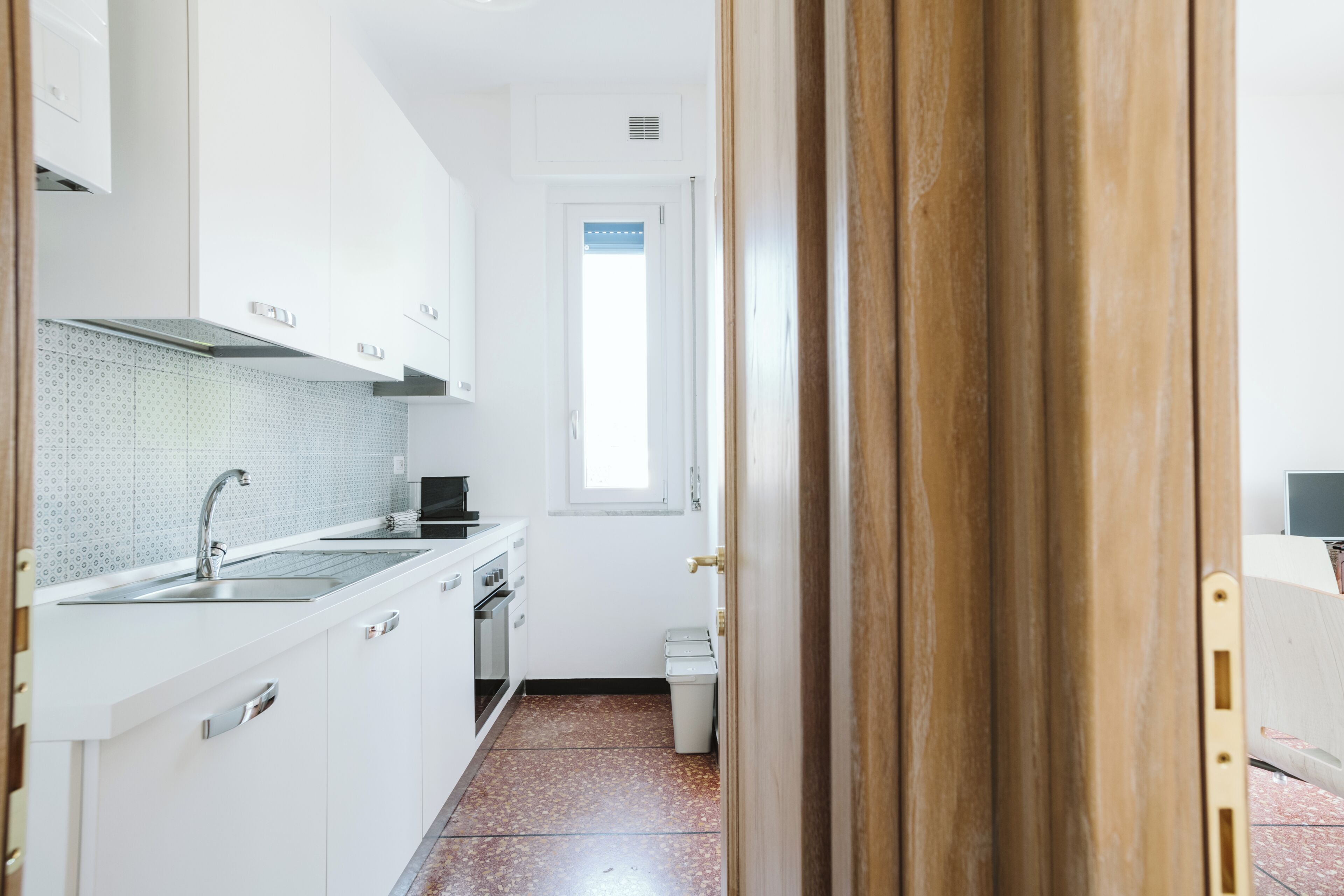 A kitchen with white cabinets, a stainless steel sink, and a tiled backsplash.