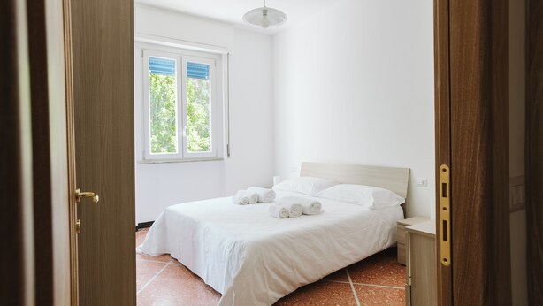 Un dormitorio con cama, mesita de noche, ventana y puerta.