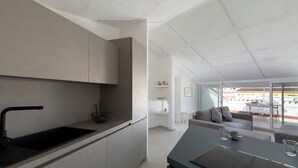 A modern kitchen with a black sink and white cabinets, a dining area with a gray sofa, and a view of the outside through large windows. - Romantic Apartment with Terrace by Wonderful Italy (Olbia)