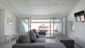 A modern living room with a grey sofa, a bench, and a flat-screen TV mounted on the wall. - Romantic Apartment with Terrace by Wonderful Italy (Olbia)