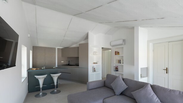 A modern living room with a grey sofa, two white bar stools, and a kitchen area in the background. - Romantic Apartment with Terrace by Wonderful Italy (Olbia)