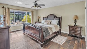 A bedroom with a large bed, a ceiling fan, a window with curtains, a nightstand with a lamp, and a dresser. - beautiful and safe golf neighborhood.
 10 minute from downtown and the beach (St. Petersburg)