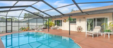 A covered swimming pool with a geometric roof structure, surrounded by outdoor furniture and potted plants.