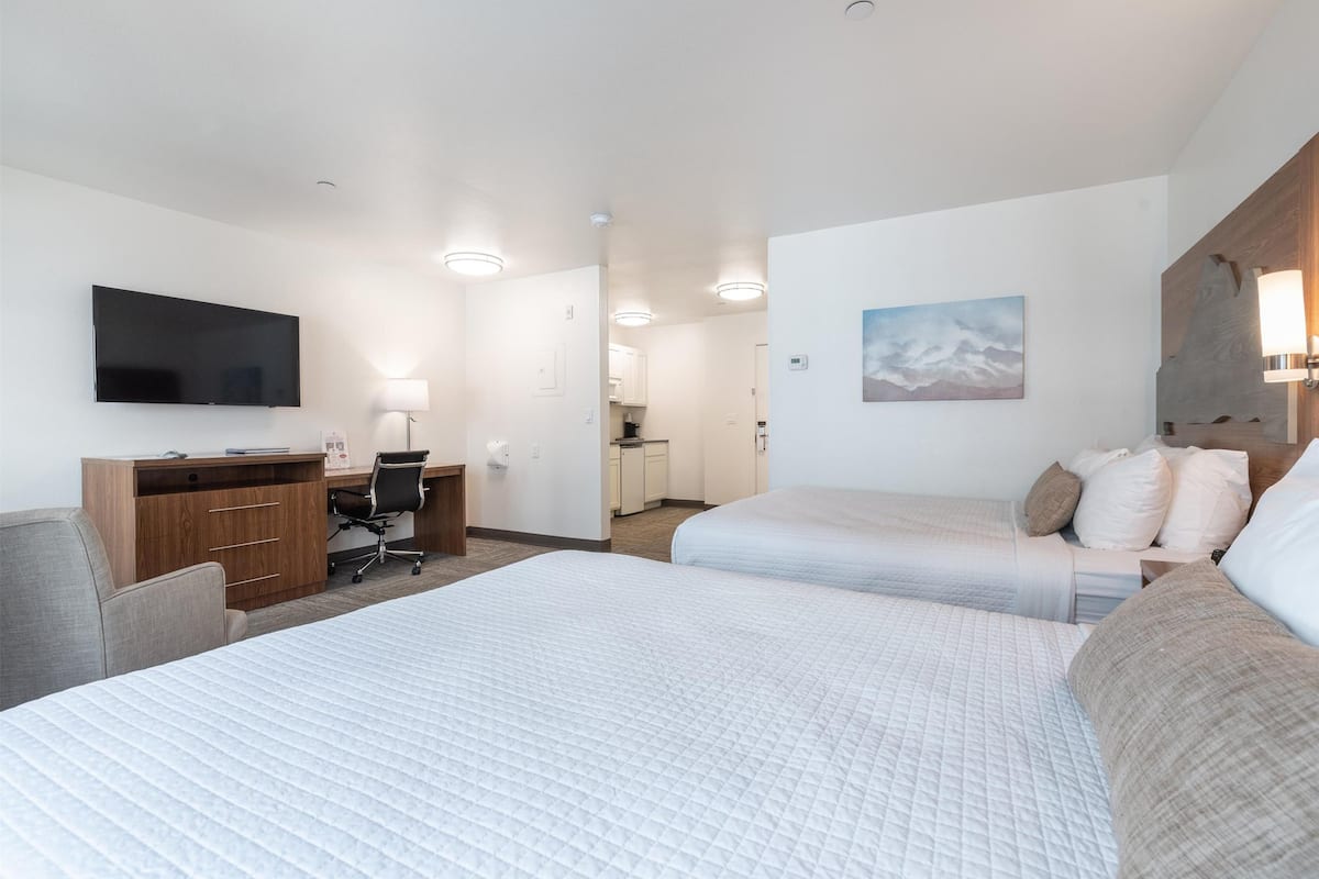 Une chambre d’hôtel avec deux lits, un bureau, une chaise, une télévision et un tableau au mur.