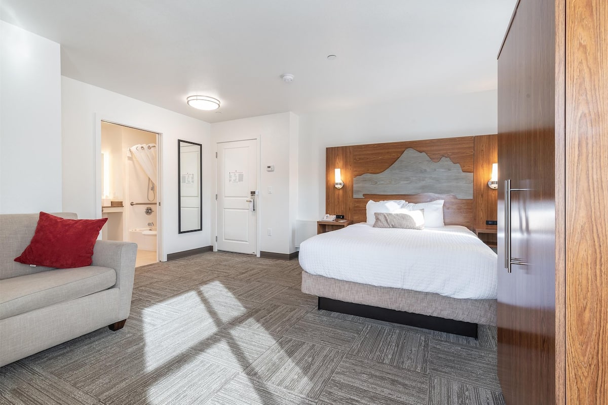 Une chambre d’hôtel avec un lit, un canapé, une tête de lit en bois et une armoire.