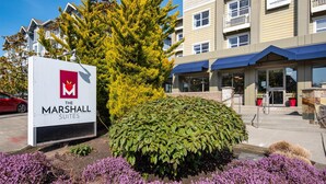 Une enseigne pour « The Marshall Suites », un immeuble doté d’un auvent bleu, avec un grand arbre devant.