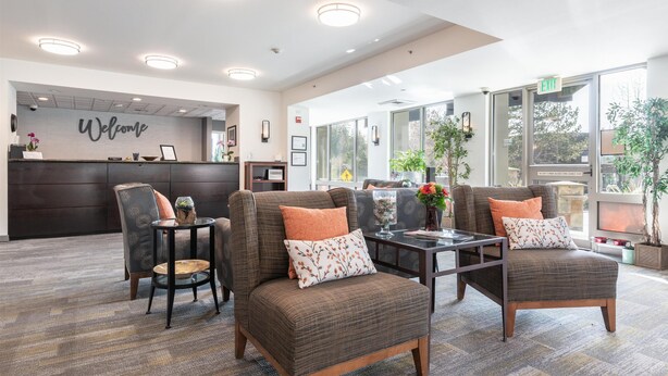 Un espace d’accueil avec une pancarte « Bienvenue », deux fauteuils ornés de coussins à motifs floraux, une petite table et une plante en pot.