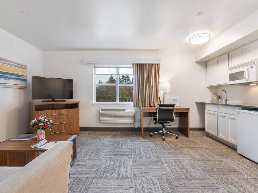 Une chambre d’hôtel avec un bureau en bois, une télévision, un coin cuisine et une fenêtre avec des rideaux.