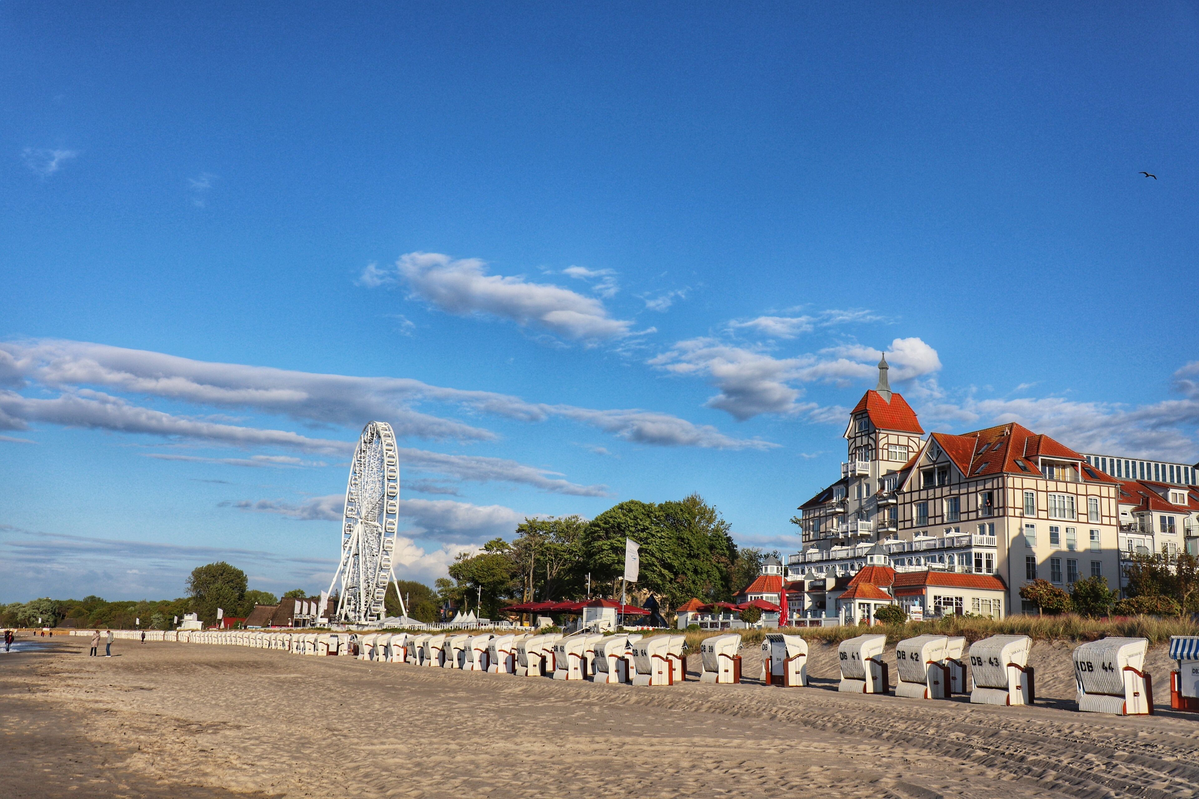 Un hotel sul lungomare con una ruota panoramica, un edificio grande con tetto rosso e una fila di cabine.