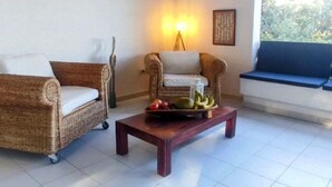 Uma área de estar acolhedora com dois sofás de vime, uma mesa de centro de madeira com frutas e uma luminária fixada na parede.