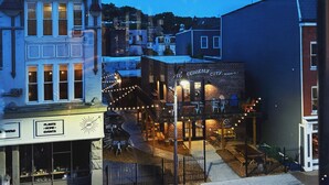 A street view at dusk with buildings, a sign for 'The Final Tour', and outdoor seating areas.