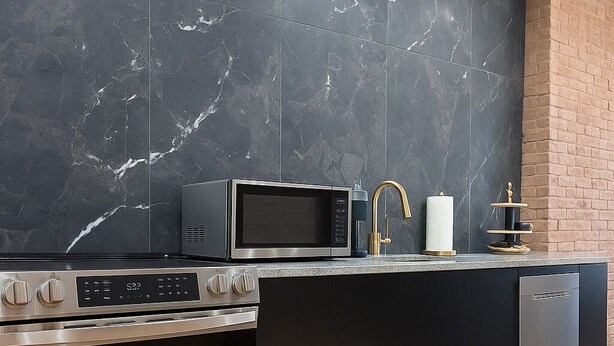 A modern kitchen with a black marble backsplash, stainless steel appliances, and a brick accent wall.