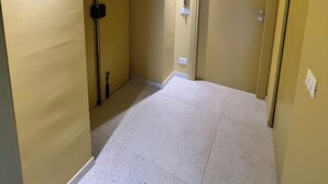 A narrow hallway with beige walls and white speckled flooring. There is a door on the right and a light fixture on the left. - Fermata Marconi two-room apartment in the center of Turin (Torino)
