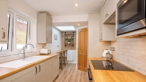 A compact kitchen with a wooden countertop, a built-in oven, a microwave, and a window with blinds. - The Granville, 4 bedroom house, sleeps 7 (York)