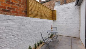 A small patio with a table and chairs, a bottle of champagne, and a white brick wall. - The Granville, 4 bedroom house, sleeps 7 (York)