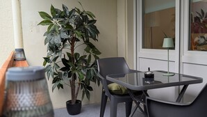 Un petit balcon avec une table, des chaises, un pot de fleurs et une fenêtre donnant sur un beau paysage.
