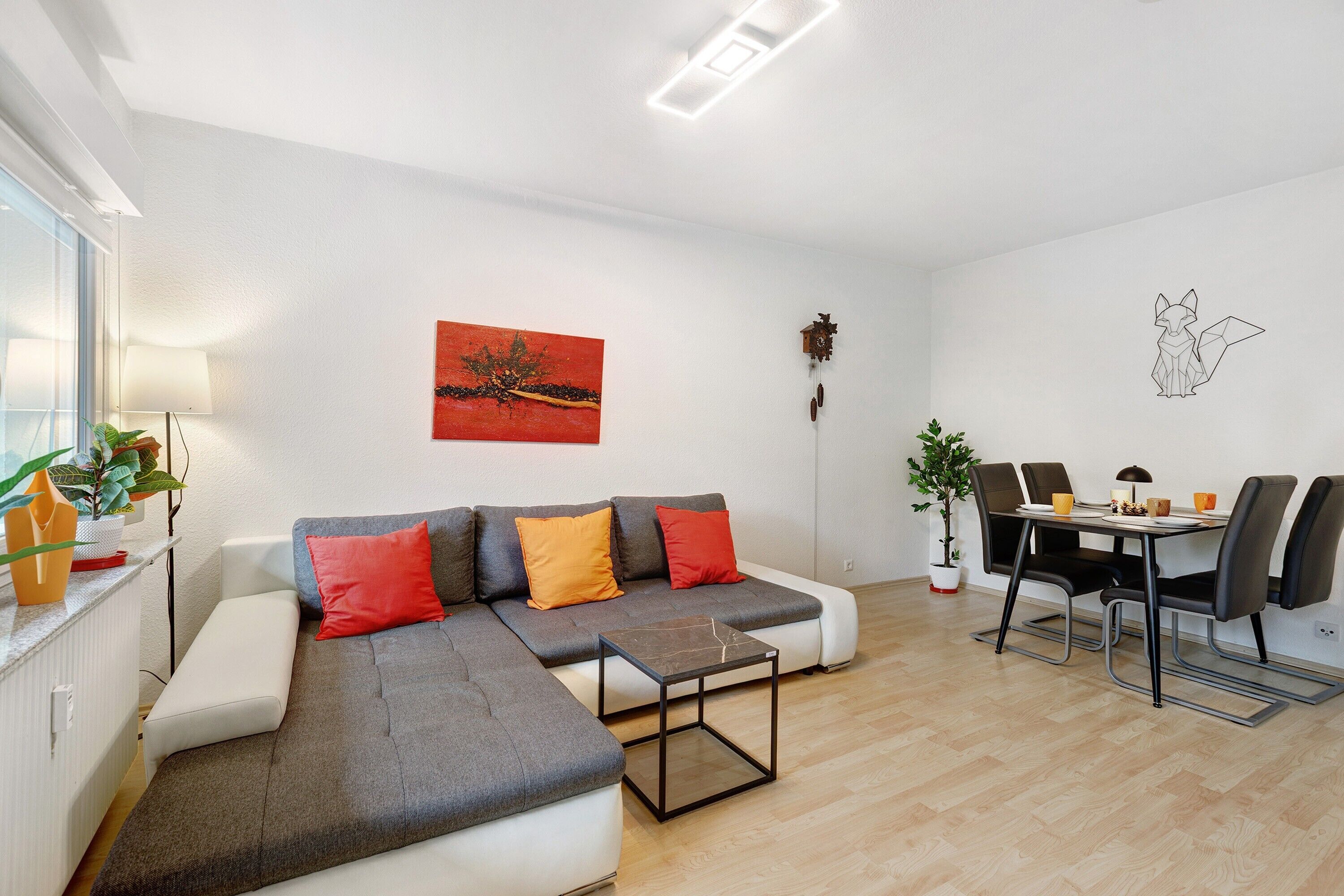Un salon moderne comprenant un canapé d’angle, une table à manger avec des chaises, une table basse et une horloge murale.