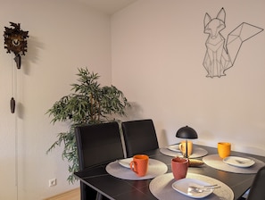 Un comedor con una mesa dispuesta para dos personas, una planta en maceta, un reloj de pared e ilustración de un zorro.