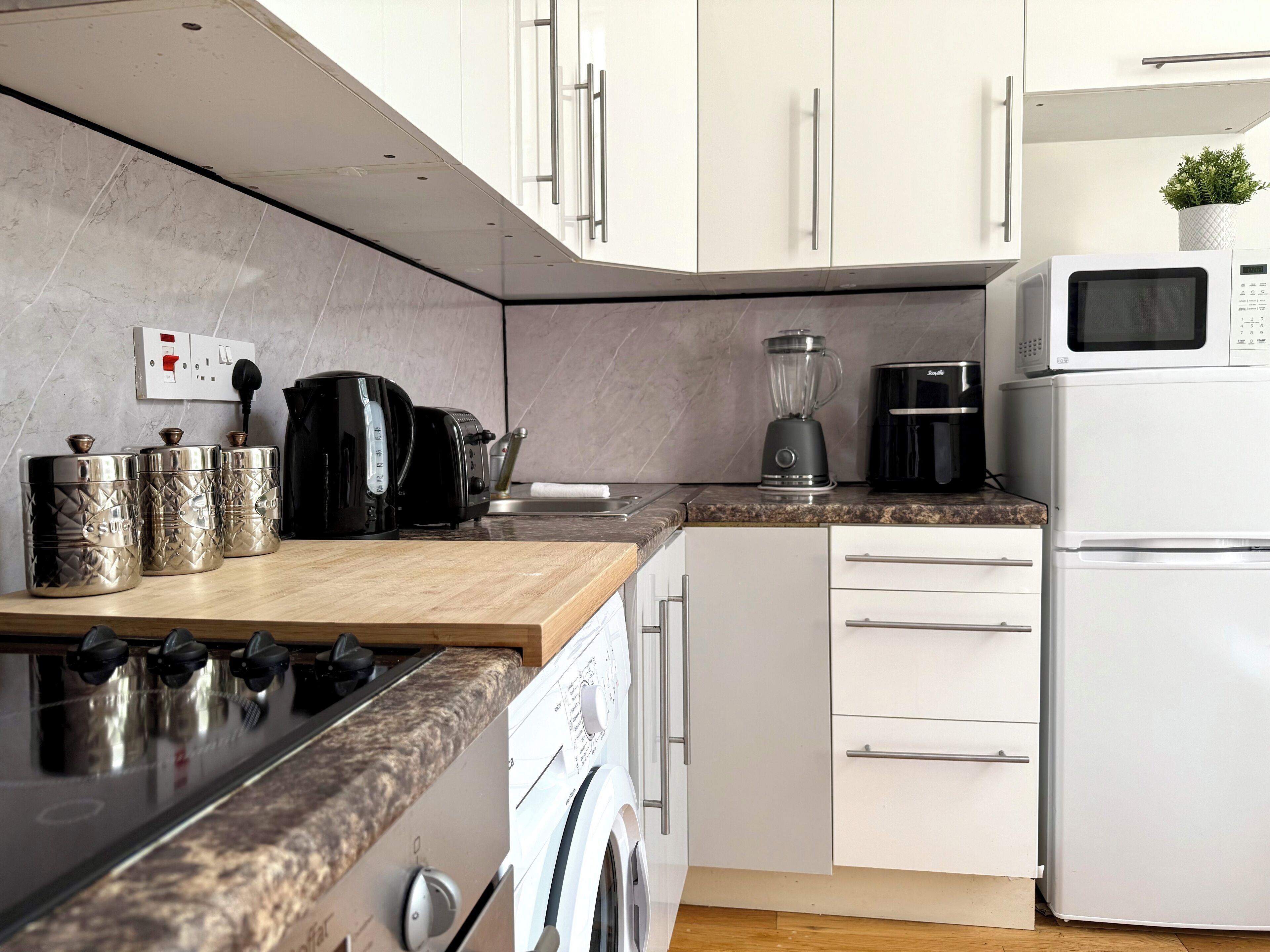 A modern kitchen with a gas stove, microwave, coffee maker, blender, and a washing machine.