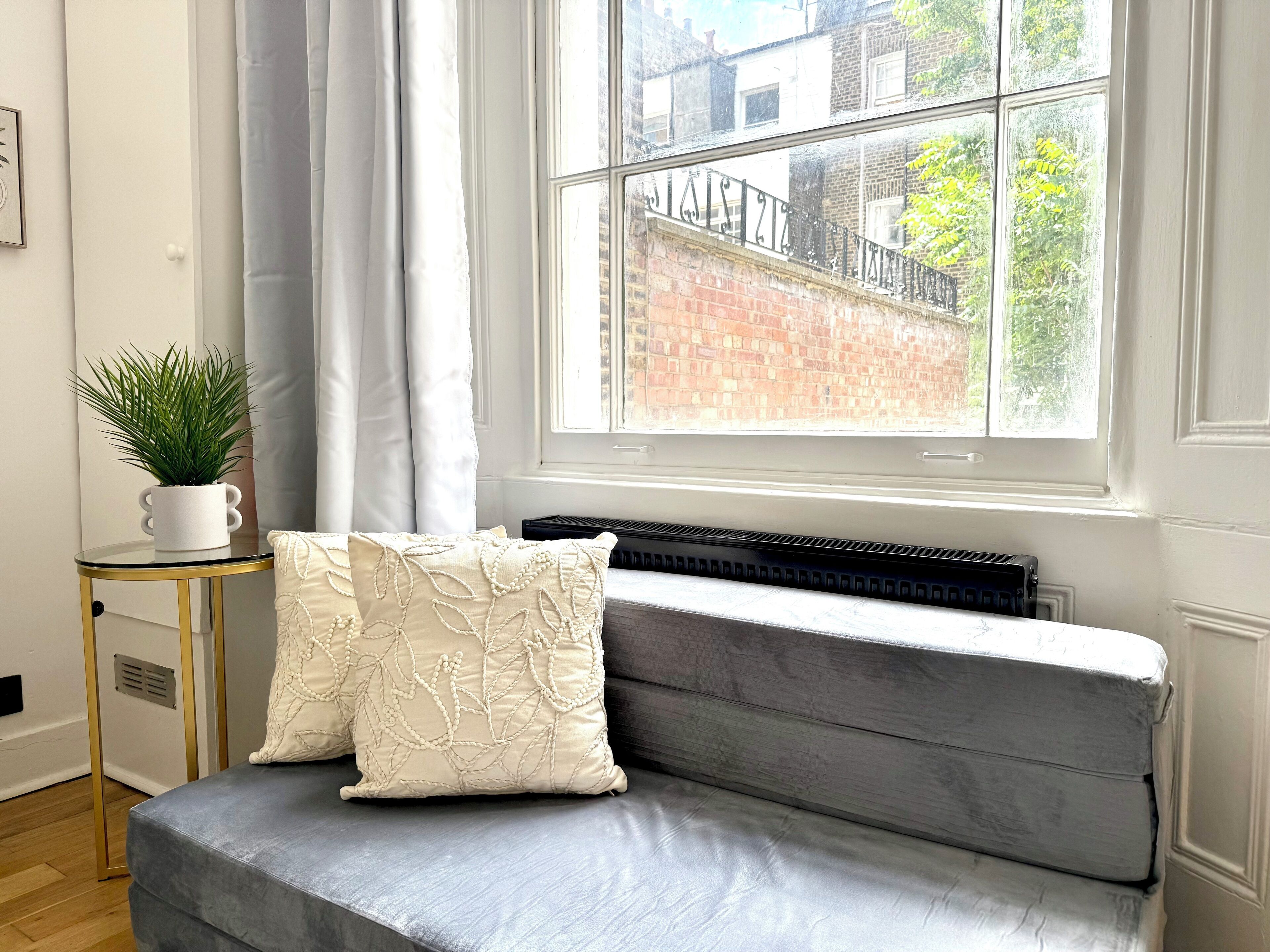 A room with a grey sofa, white cushions, a small white plant, and a radiator.