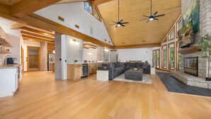 A spacious living area with a wooden ceiling, a stone fireplace, and a large TV mounted on the wall. - The Manor-Indoor Pool-Speak Easy-Game Room-Sauna (Bentonville)