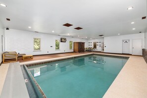 An indoor swimming pool with a tiled edge, wooden benches, and a ceiling with recessed lighting. - The Manor-Indoor Pool-Speak Easy-Game Room-Sauna (Bentonville)