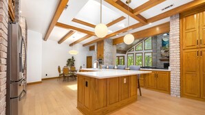 A spacious kitchen with a large island, wooden cabinets, and a stone accent wall. - The Manor-Indoor Pool-Speak Easy-Game Room-Sauna (Bentonville)