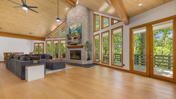 A spacious living room with a stone fireplace, large windows, and a high ceiling. - The Manor-Indoor Pool-Speak Easy-Game Room-Sauna (Bentonville)