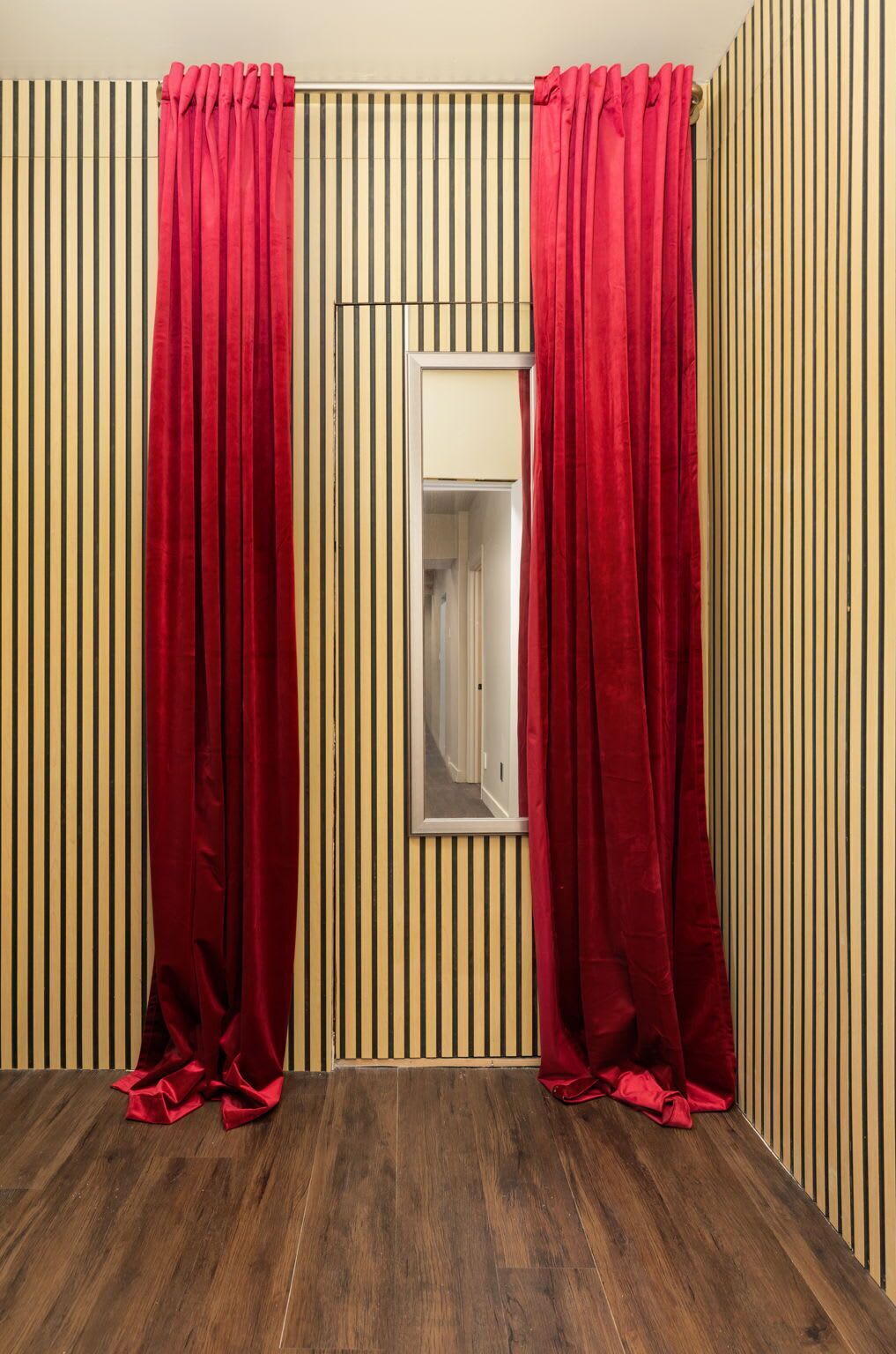 A room with a wooden floor, a window with a white frame, and red curtains.