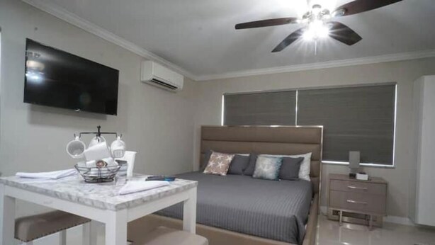 A bedroom with a bed, a desk, a chair, a TV, a ceiling fan, and a window. - Modern Beach Studio 3 (Pompano Beach)