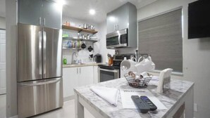 A modern kitchen with stainless steel appliances, a marble countertop, and a welcome mat. - Modern Beach Studio 3 (Pompano Beach)