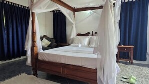 Ein Himmelbett mit hölzernem Gestell und weißer Bettwäsche, ein Nachttisch mit Lampe und dunkelblaue Vorhänge.