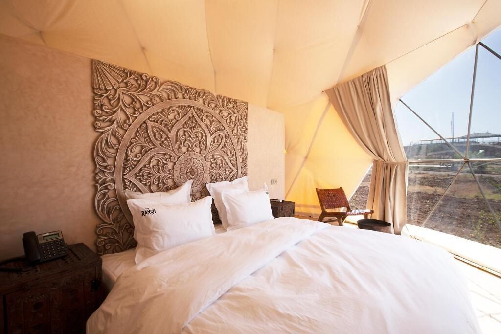 Un dormitorio con una cama grande, cabecera con intrincados detalles tallados, mesita de noche con teléfono y vista al exterior a través de una ventana.
