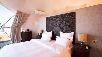 Una habitación de hotel con una cama grande, un cabecero decorativo, lámparas de noche y vistas a través de una ventana con cortinas.