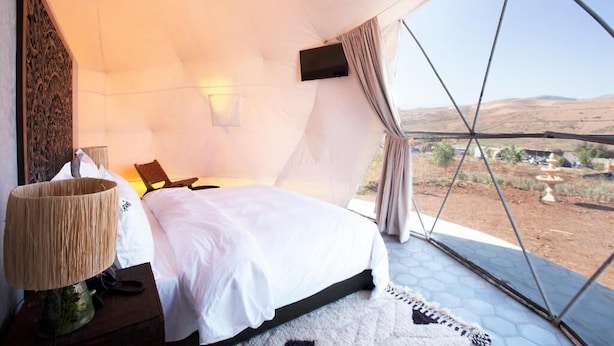A bedroom with a large bed, a hanging chair, a lamp, and a view of the landscape.